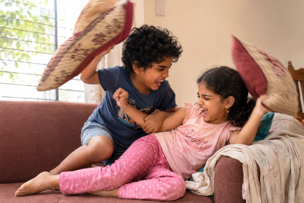Brother and sister laughing during a playful sofa cushion fight
