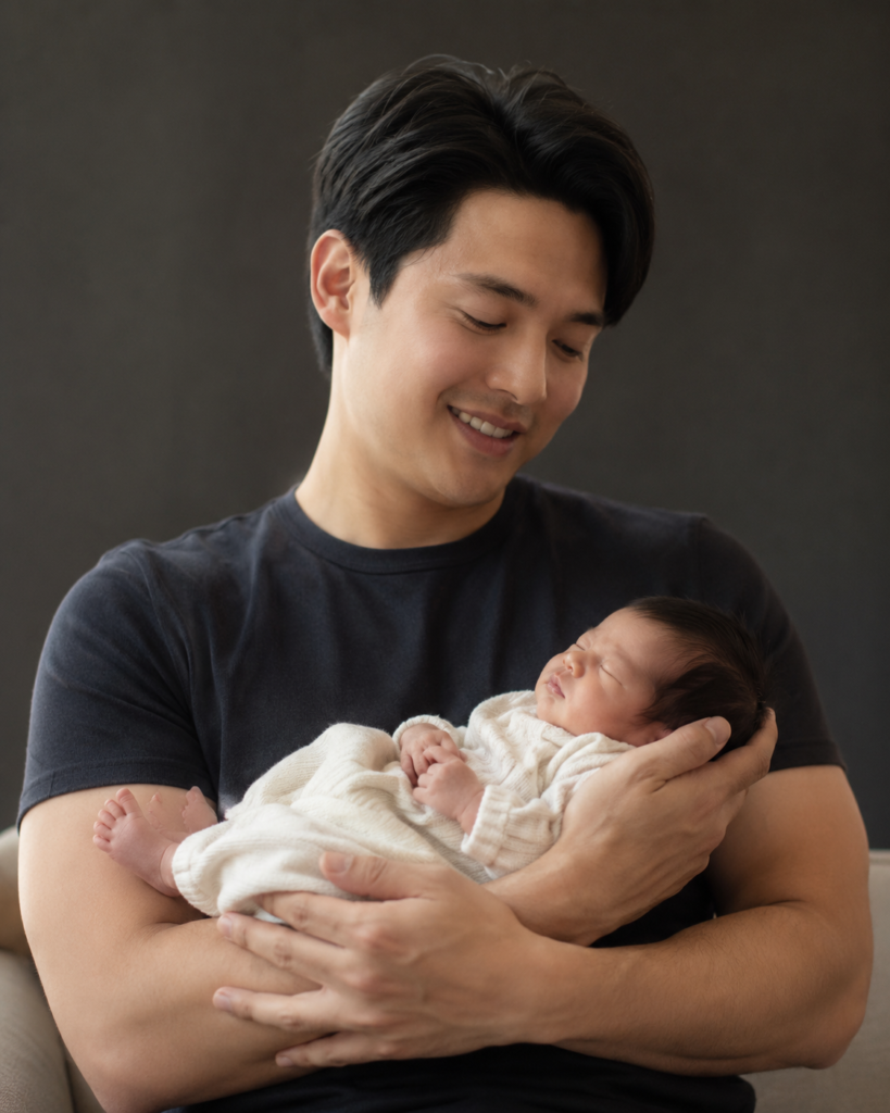 Father gently cradling his newborn daughter in his arms under soft window light