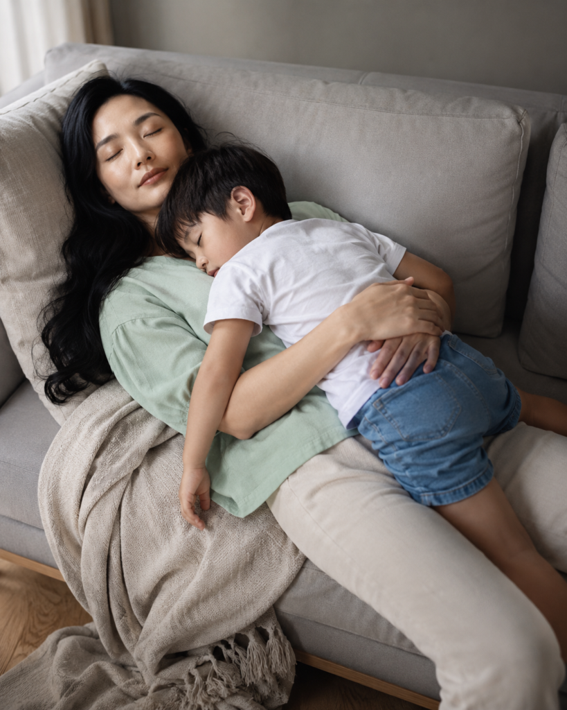 Mother resting on a sofa with her toddler son asleep on her chest